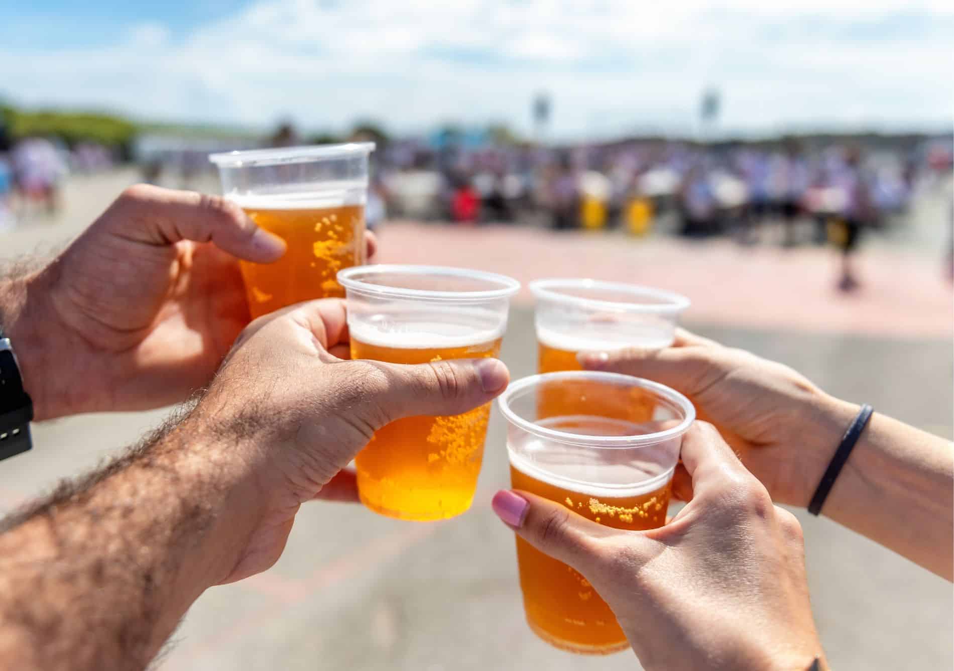 four people holding up plastic cups of beer at a festival