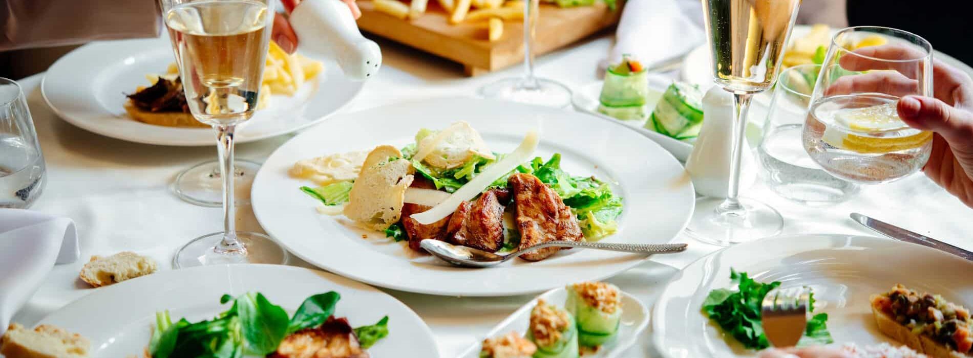 Restaurant table full of dishes of food and glasses of wine.