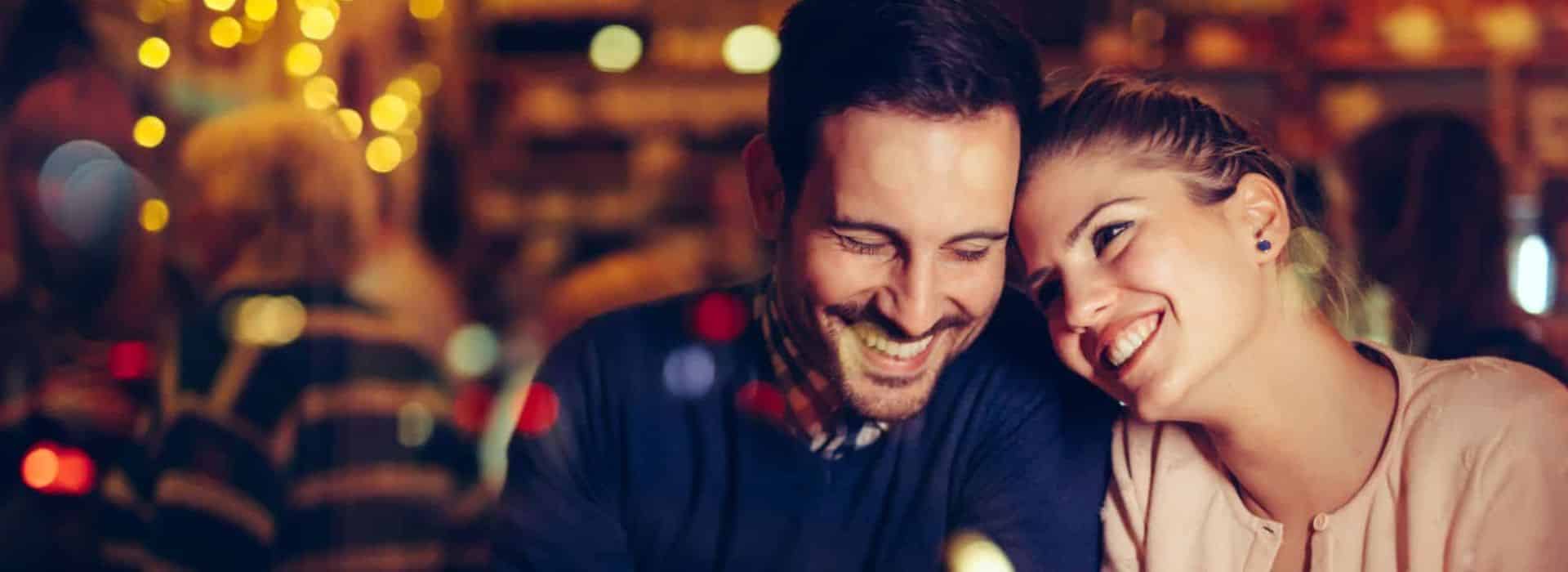 couple snuggling at a bar on a date night. cups of coffee and candle in front of them.