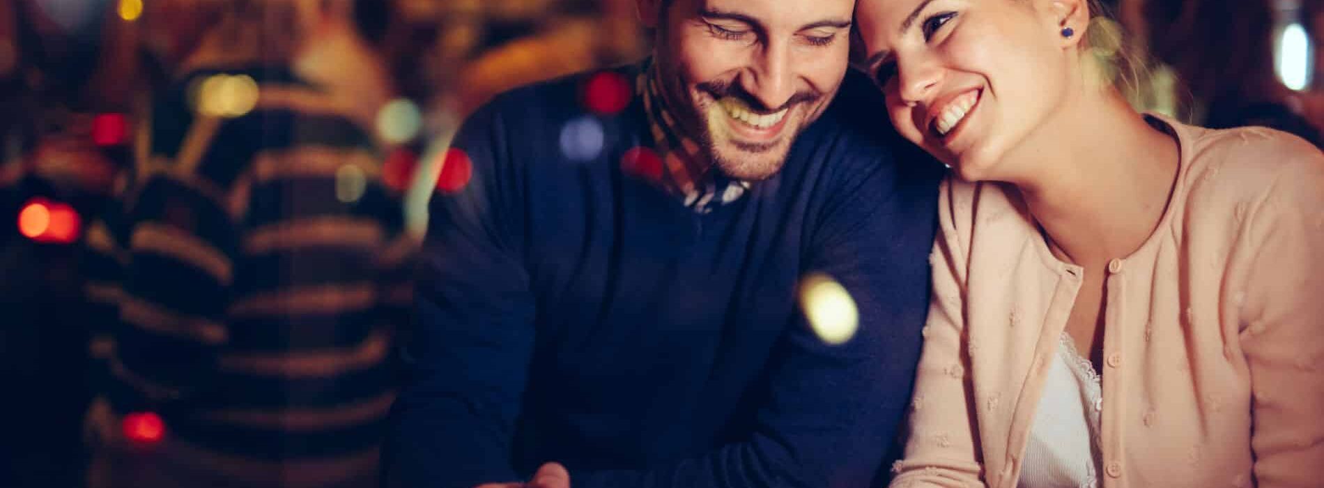 couple snuggling at a bar on a date night. cups of coffee and candle in front of them.