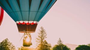 couple with tour guide on hot air balloon ride over trees at sunrise