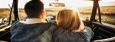 view from behind of couple sitting in car embracing and driving into the sunset