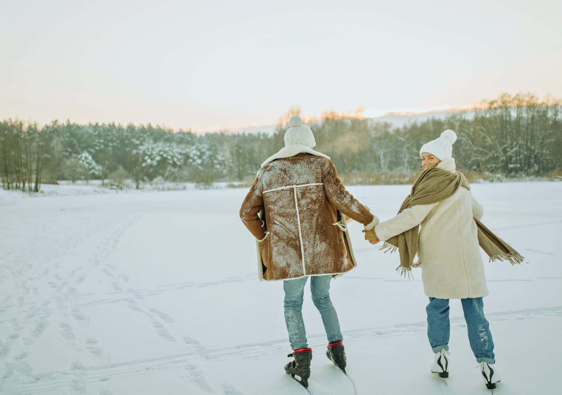 couple holding hands skating on forest lake