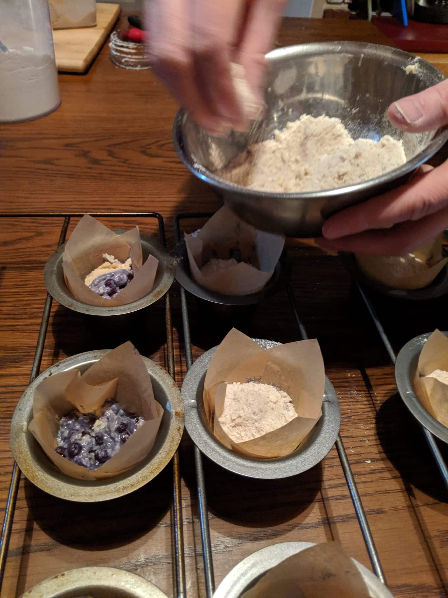 muffin batter in tins with crumb topping being added