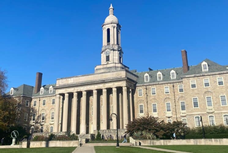 A large brick college building with columns and a tall spire against a blue sky