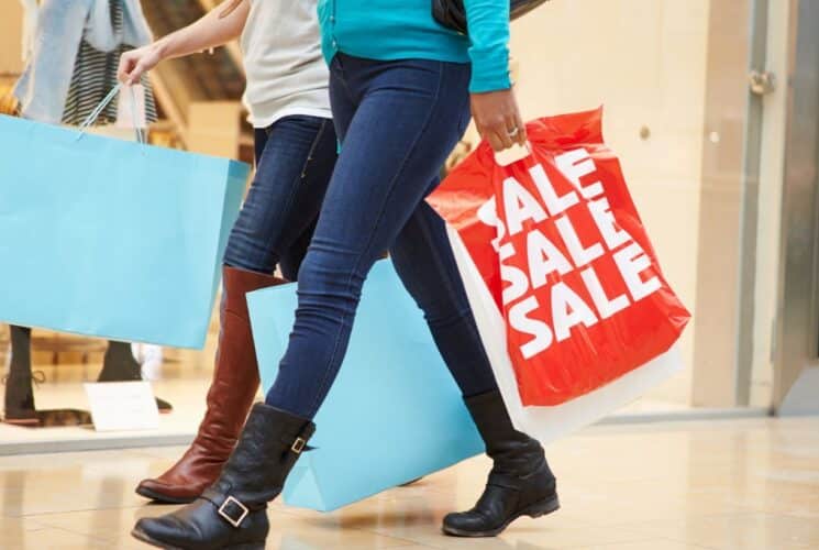 Two ladies wearing jeans and boots and holding shopping bags walking in a mall