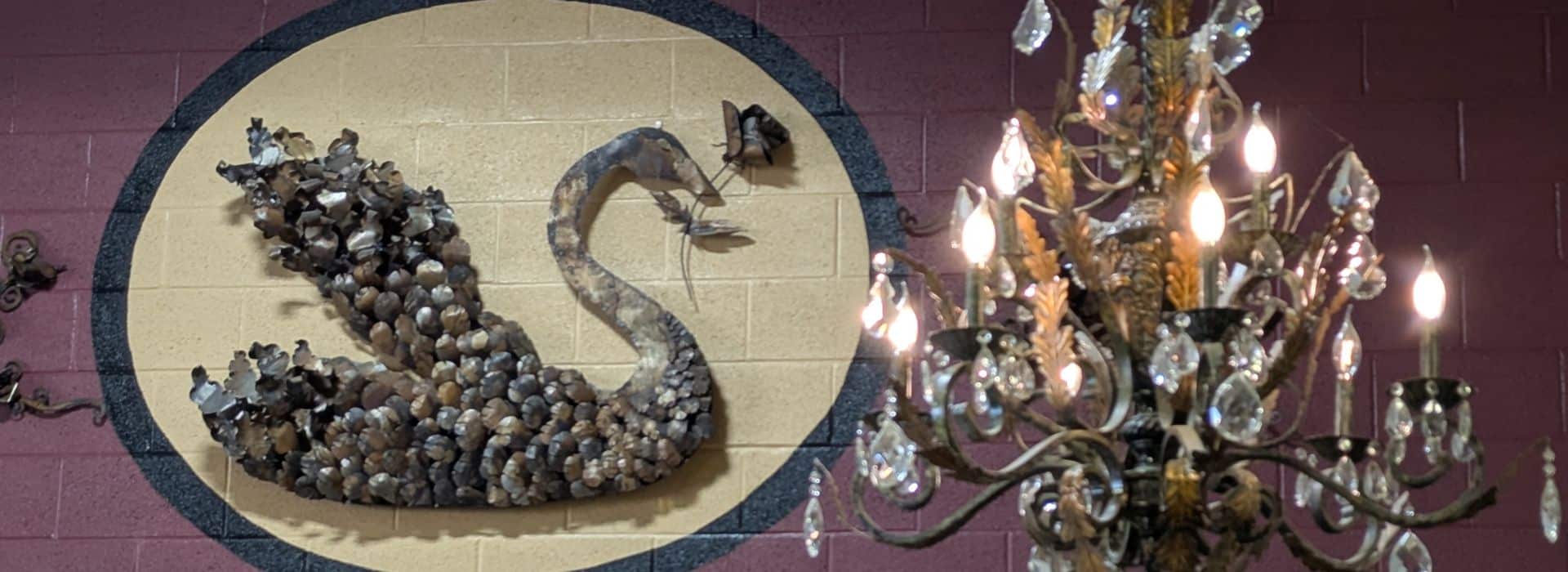 wall with a swan holding a rose in its beak and a chandelier to the right in the foreground.