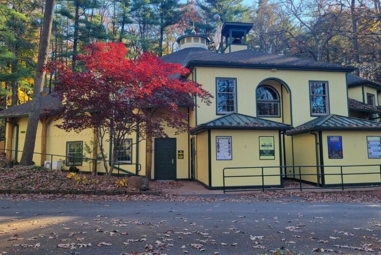 A yellow theatre with black trim nestled in the woods during the fall season