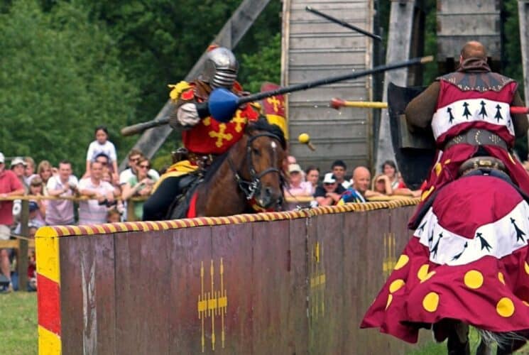 Two people riding horses along a fence in a jousting competition at a Renaissance faire