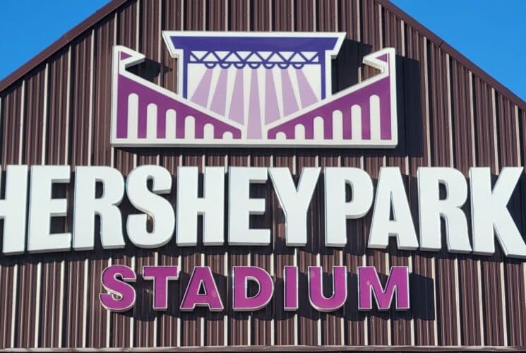 Large white, pink and purple sign for a stadium on brown A-frame siding