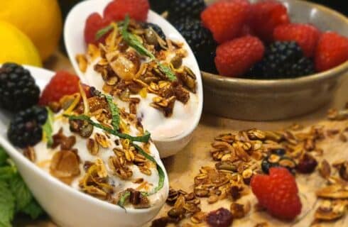 Two white slanted bowls of yogurt topped with granola and berries