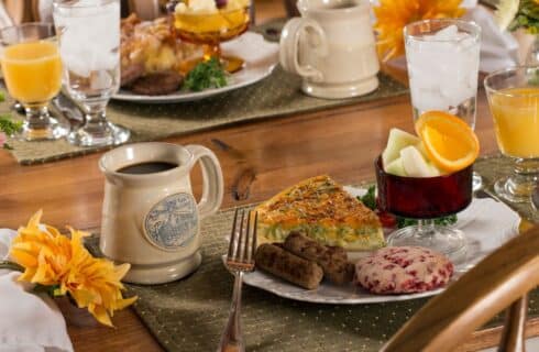 A wood table with two places set for breakfast with plates of food, cups of fruit, glasses of orange juce and ceramic mugs of coffee