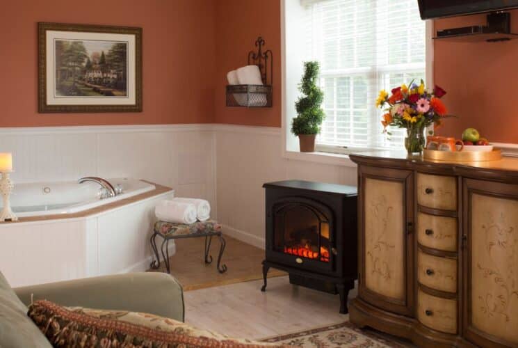 Bathroom with corner jacuzzi tub, electric fireplace, sitting chair, dresser and bright window