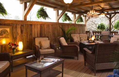 Covered deck with wicker patio furniture with striped cushions, fire table, six hanging ferns