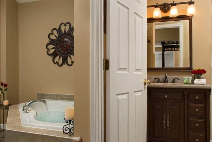 Corner jacuzzi tub filled with water, candles, bucket of white towels next to doorway into a bathroom