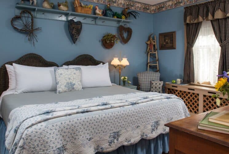 Bedroom with blue walls, king bed with blue floral quilt, country-chic decor and window with plaid curtains