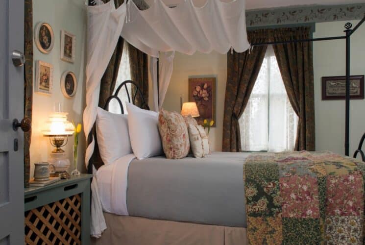 Bedroom wth queen canopy bed, floral quilt, windows with luxurious curtains