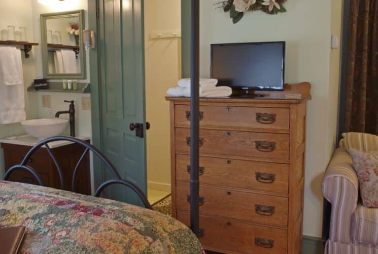 Bedroom with queen bed, loveseat, tall dresser, single sink vanity with mirror and doorway open to a shower room