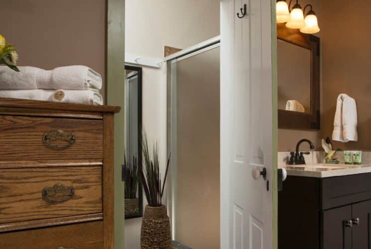 Bedroom with tall wood dresser, single sink vanity and doorway open to a shower room