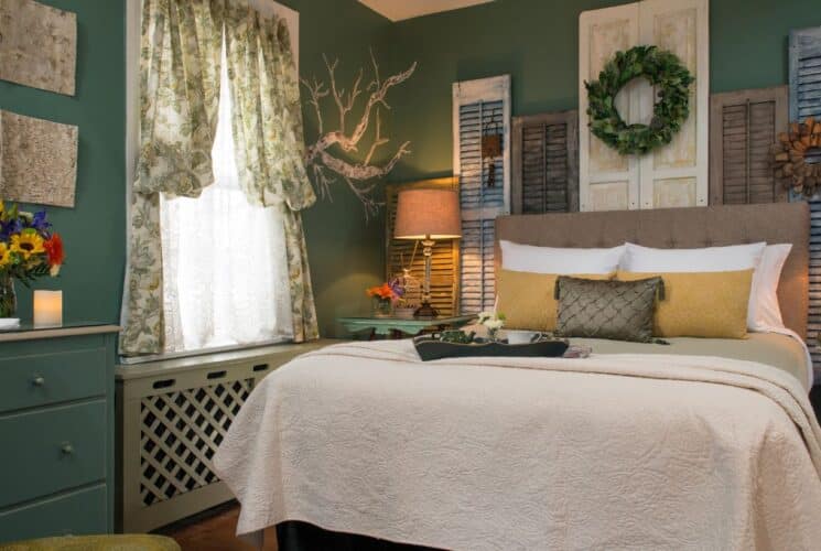 Elegant and cozy bedroom with colorful shutters behind the headboard, sitting chair and window with lace curtain