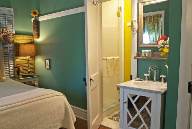 Bedroom with king bed, green walls, single sink and doorway open to a yellow bathroom