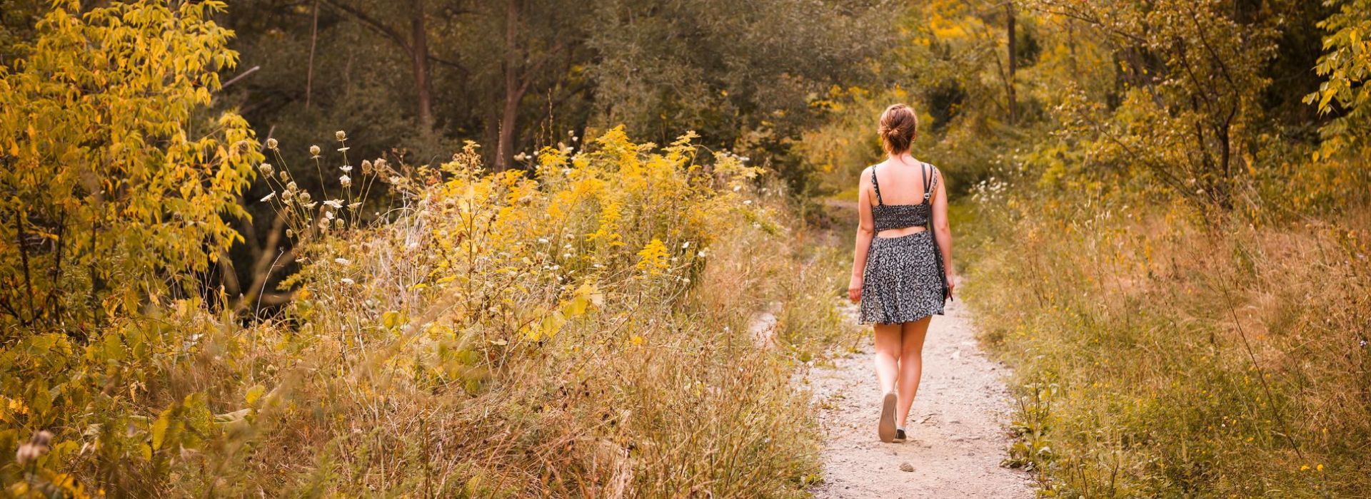 A woman in a dress is walking on a narrow path through the woods