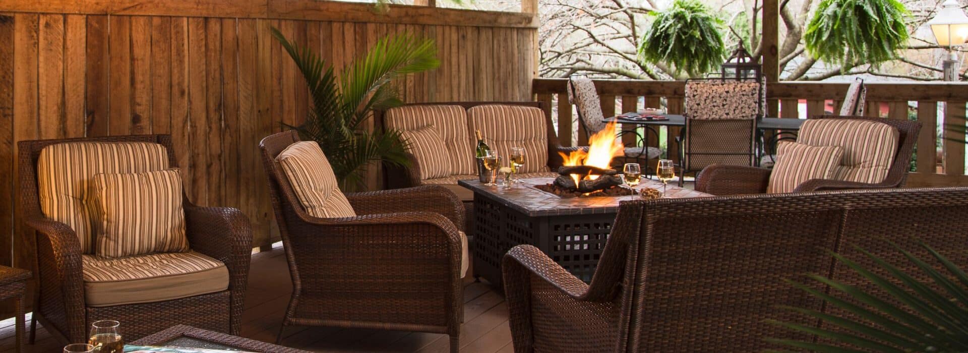 Covered deck with wicker patio furniture with striped cushions, fire table, six hanging ferns