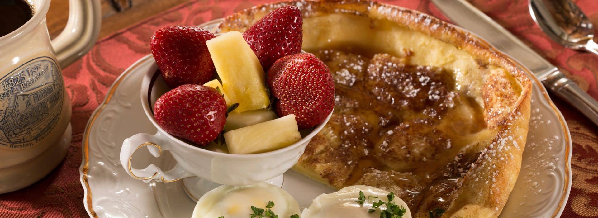 Breakfast plate with a piece of Dutch pancake, two eggs and cup of pineapple and strawberries