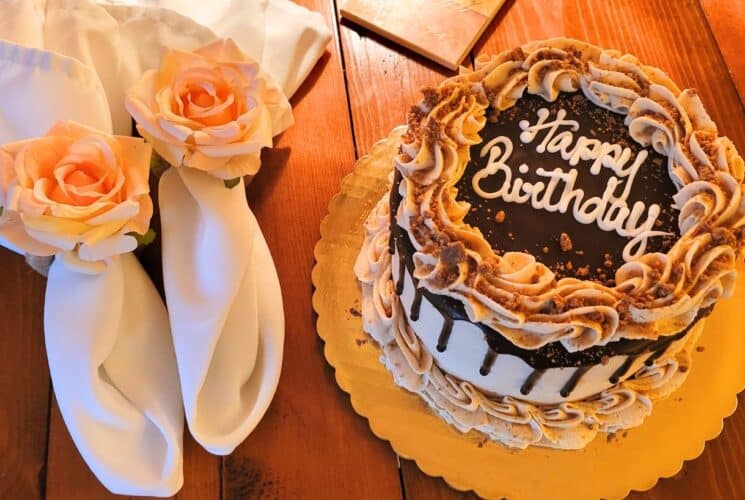 A white cake with chocolate frosting and two napkins with rose napkin holders on a wood table