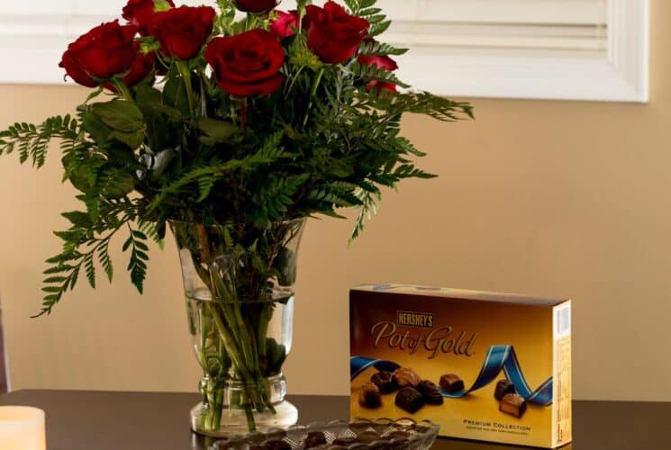 Vase of red roses, box of chocolates and candles on a brown table