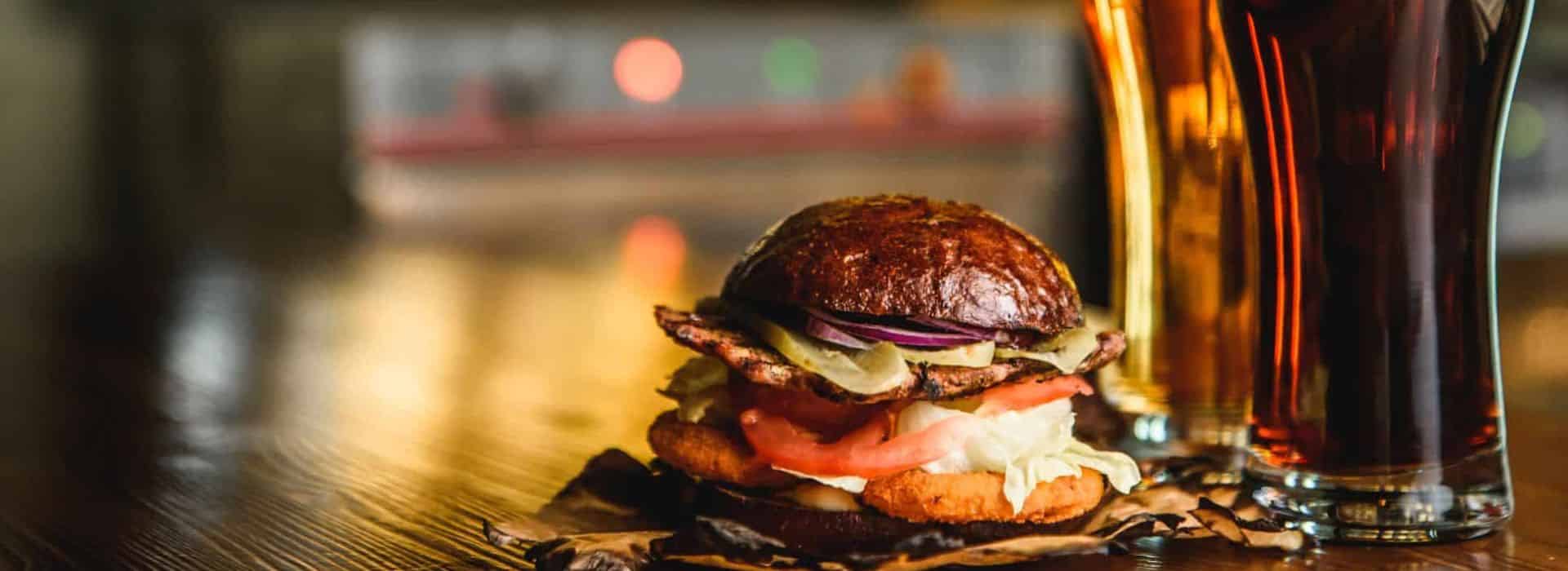 A juicy burger with two tall pints of beer on a table at a pub